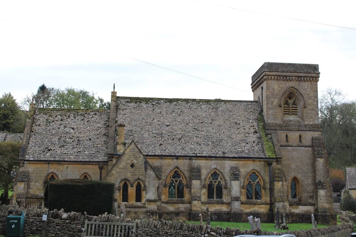 A Cotswold stone church with a squat tower behind a dry-stone wall