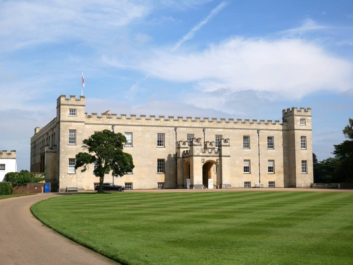 A square, battlemented stone house beyond a striped lawn