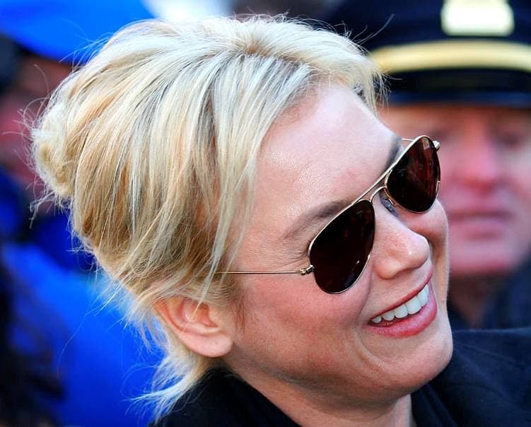 Renée Zellweger laughing in aviator sunglasses, her blonde hair pinned up