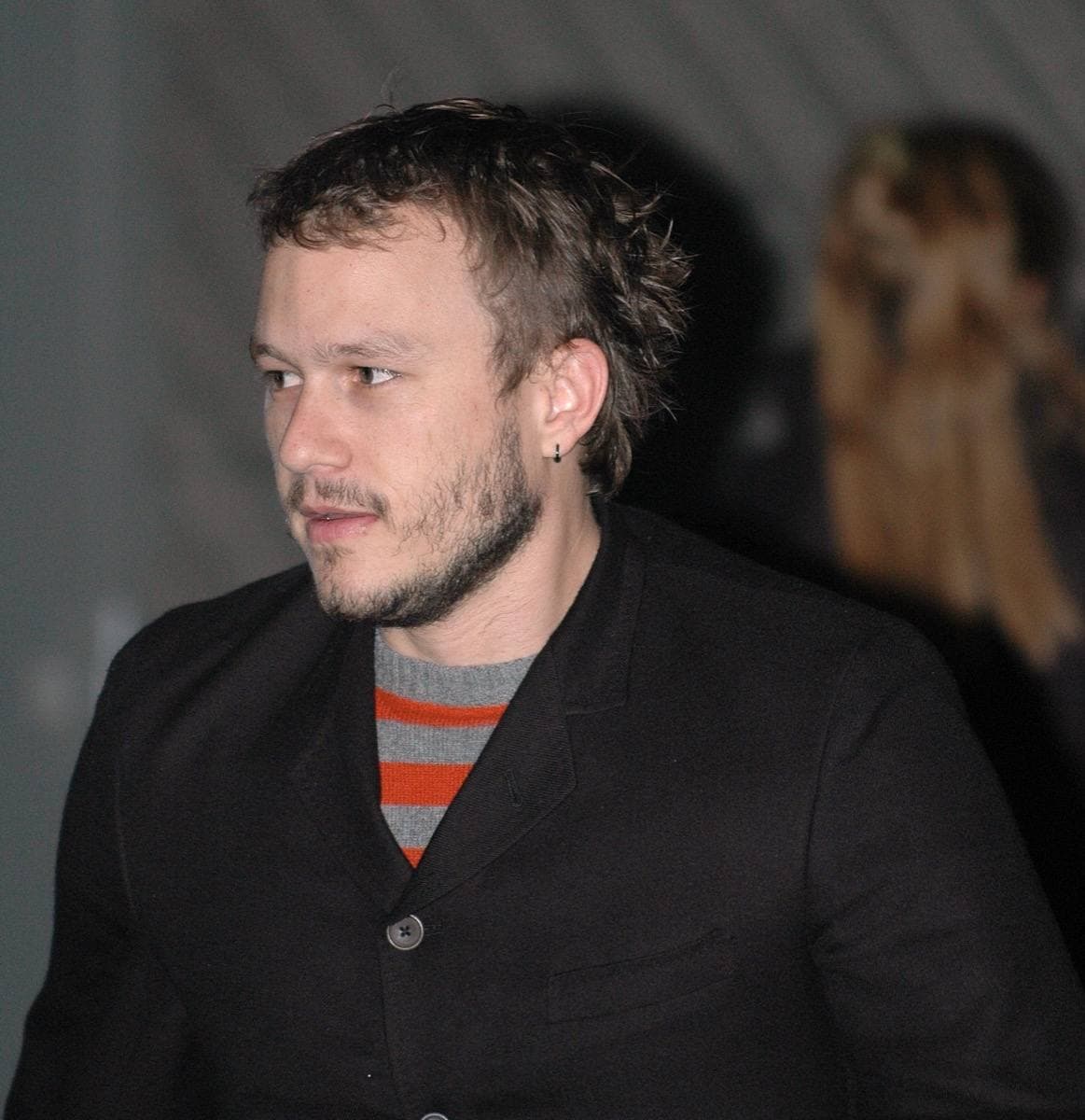 Heath Ledger, fair hair swept back, in a dark jacket, looking off to one side