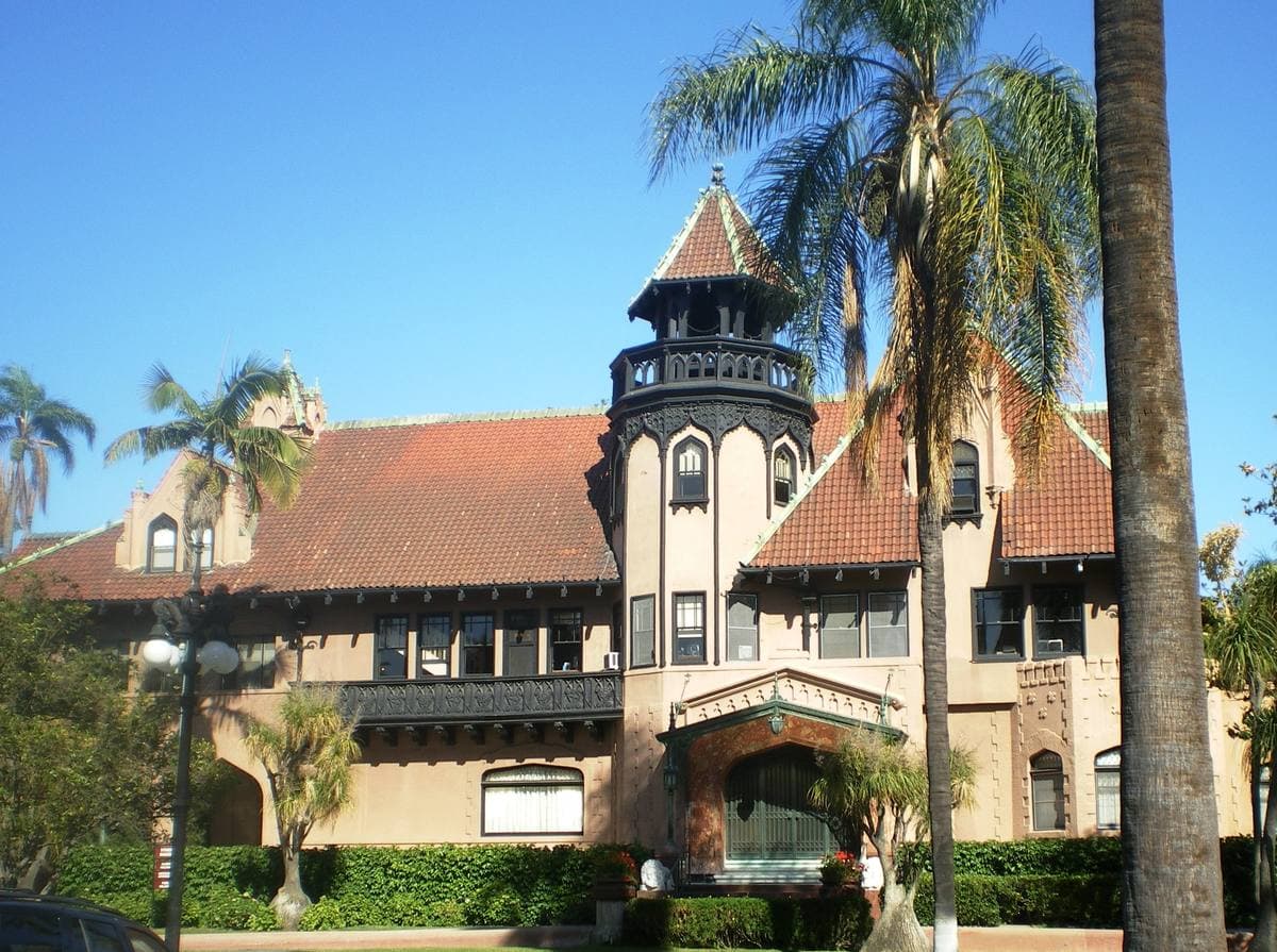 A turreted red-roofed mansion among palms and lawns
