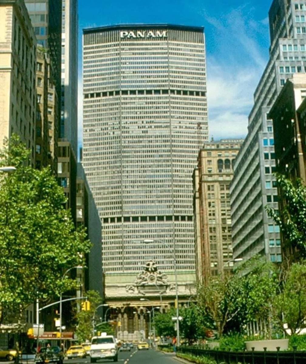 A tall, many-sided office tower closing the end of a tree-lined avenue, PAN AM in capitals at the top