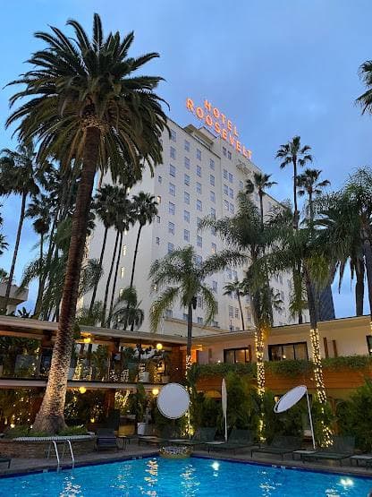 A pool lit blue at dusk, palms and a tall hotel with its sign behind