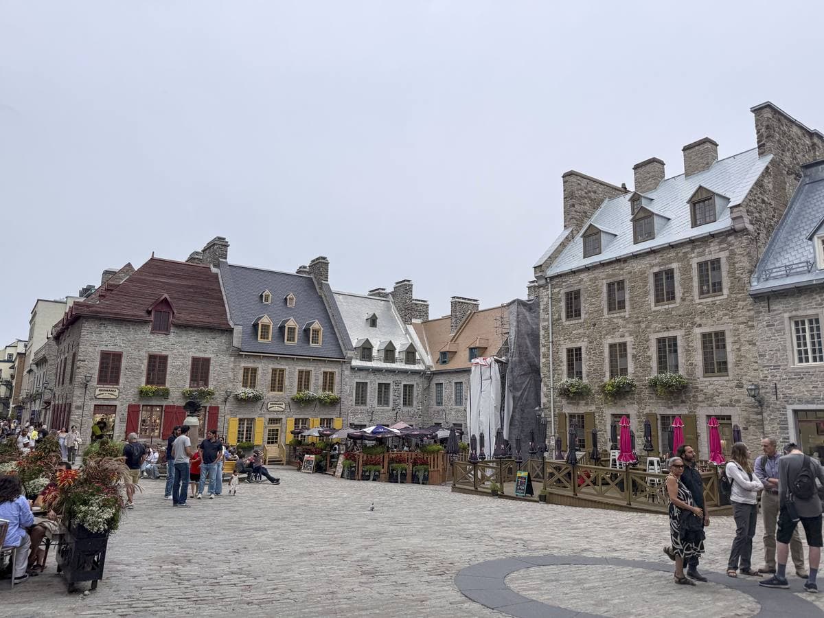 A cobbled square of grey stone houses with steep roofs and dormer windows, people walking