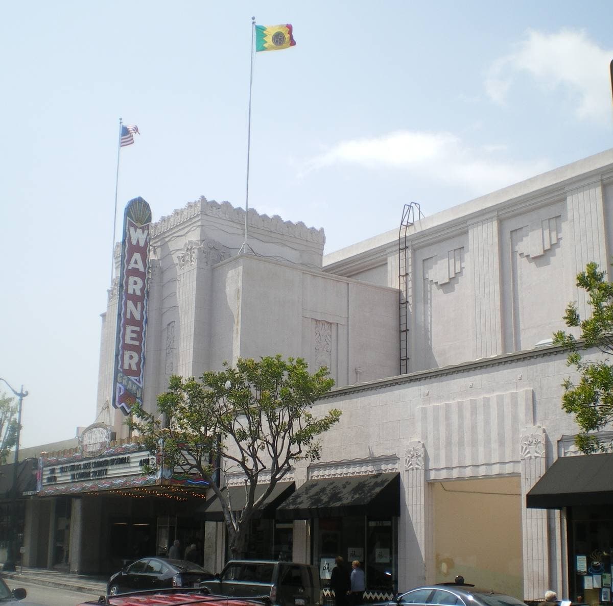 An Art Deco cinema with a tall vertical WARNER sign on a sunny street corner