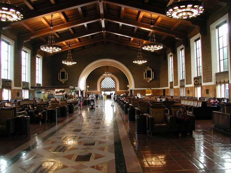 A long waiting hall with rows of armchairs, chandeliers and an arched doorway at the end