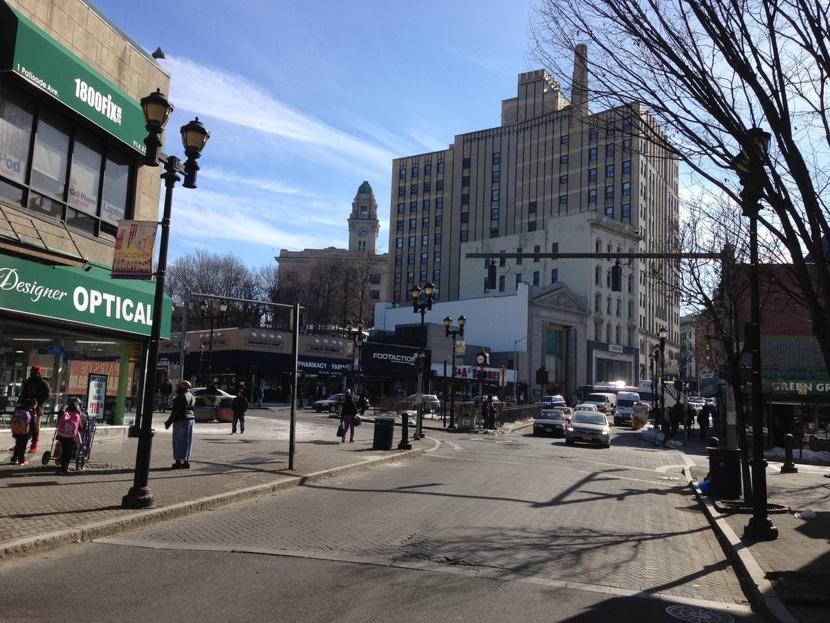 A downtown street crossing with shops, street lamps and brick towers