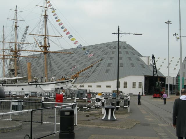 A huge ribbed timber shed over a slipway, with a ship in the foreground