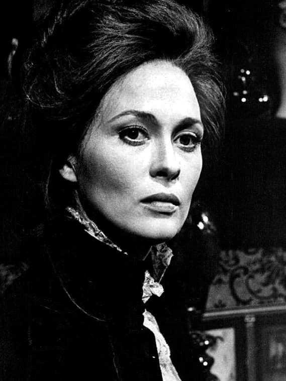 Faye Dunaway in a dark high-collared dress, looking past the camera