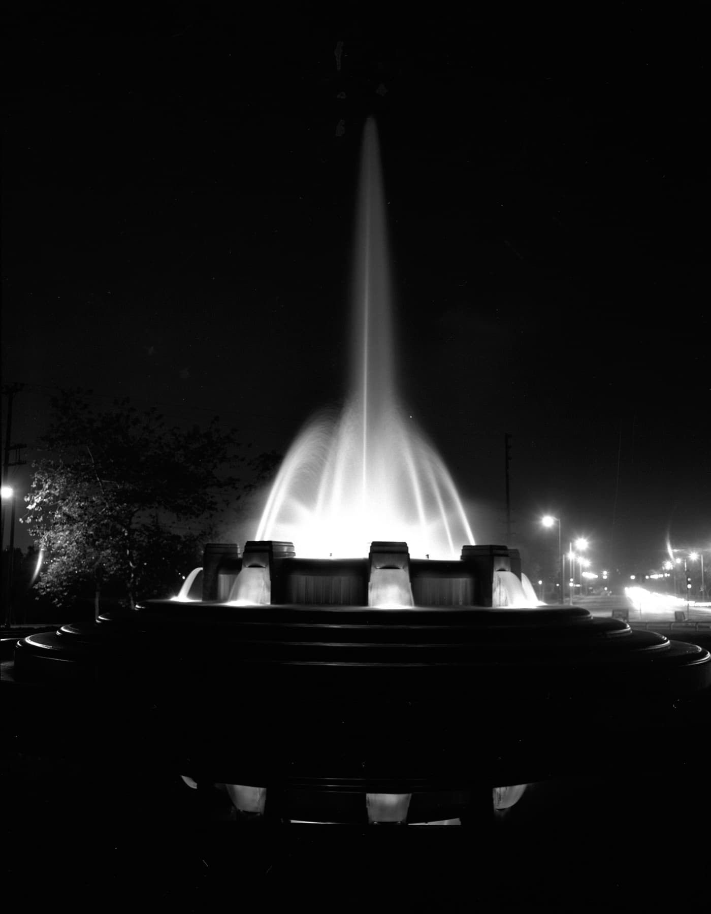 The fountain throwing a tall lit plume of water into the night