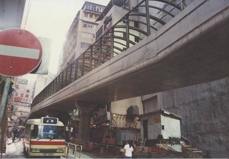 Steel framework of the covered escalator rising over a narrow street between old buildings