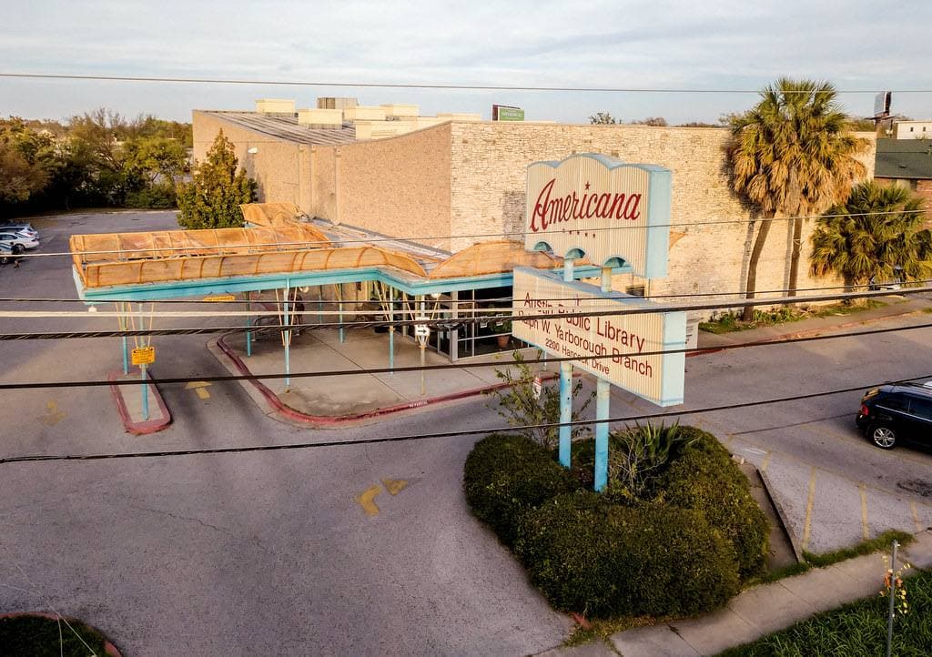 A low library building with palm trees and a mid-century Americana sign by the car park