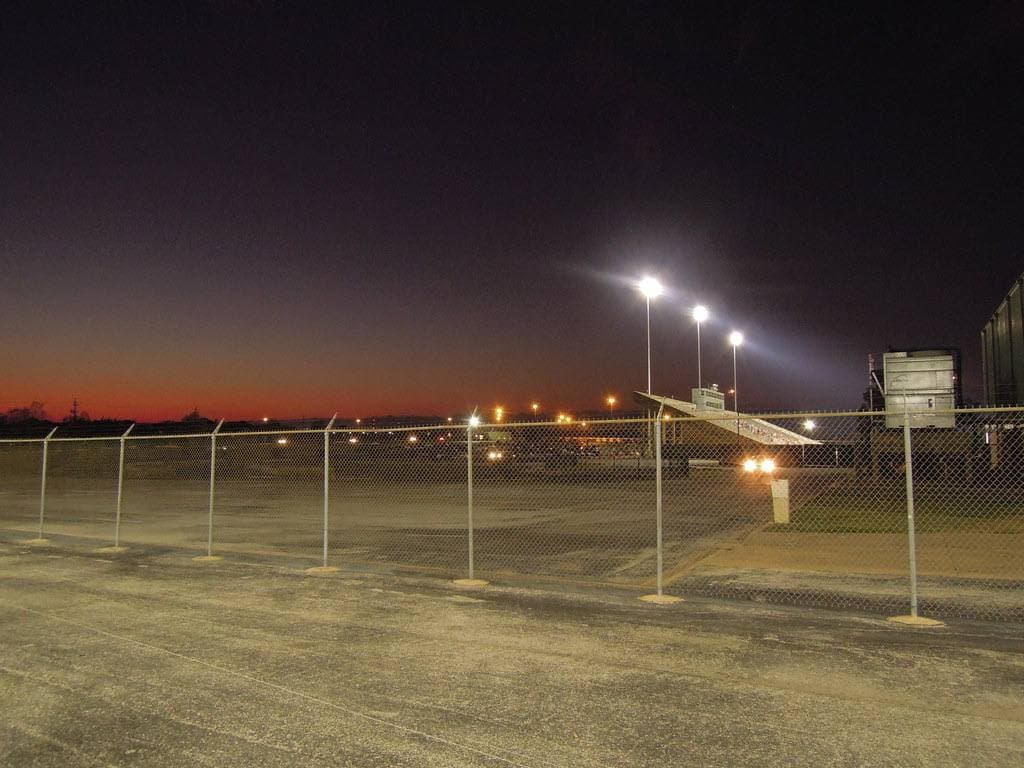 Stadium floodlights on over a fenced field under a red sky