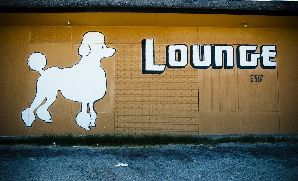 A white poodle silhouette and the word Lounge painted on a yellow brick wall