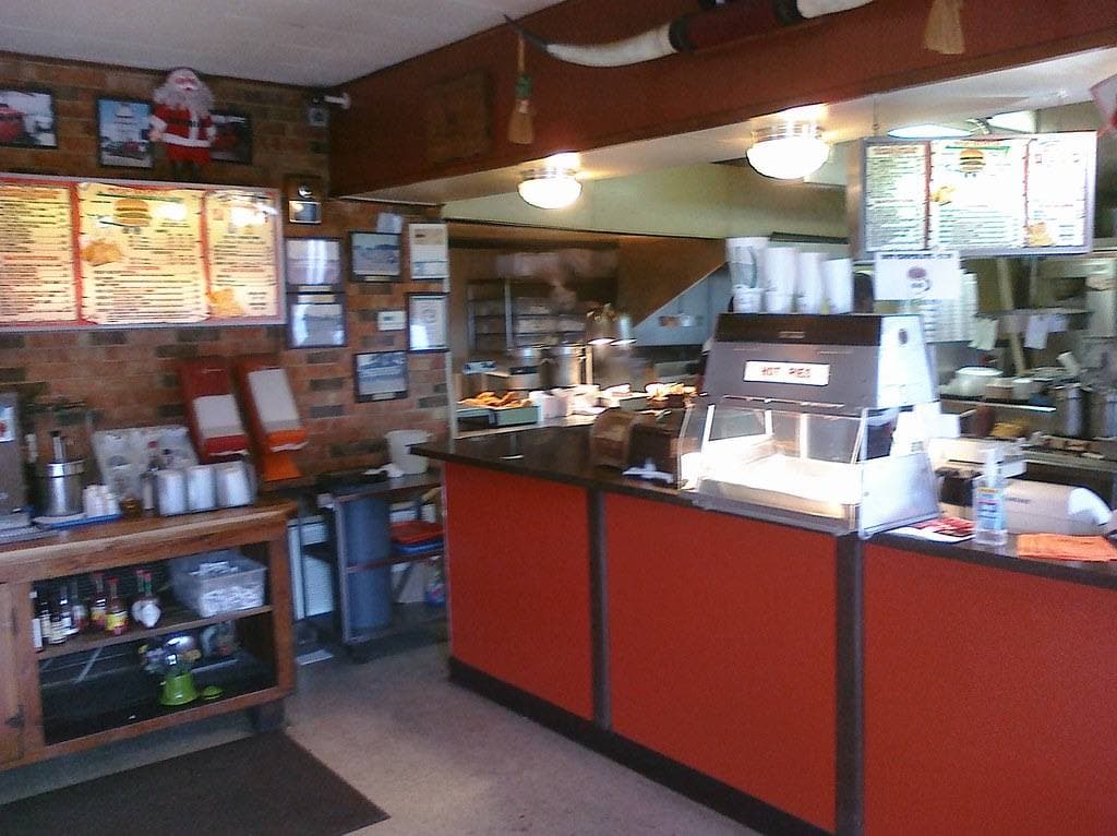 A red order counter under a lit menu board inside a burger restaurant