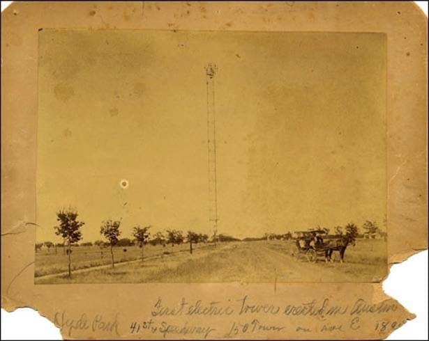 An old sepia photograph of a single thin tower rising over an empty dirt road with a horse and buggy