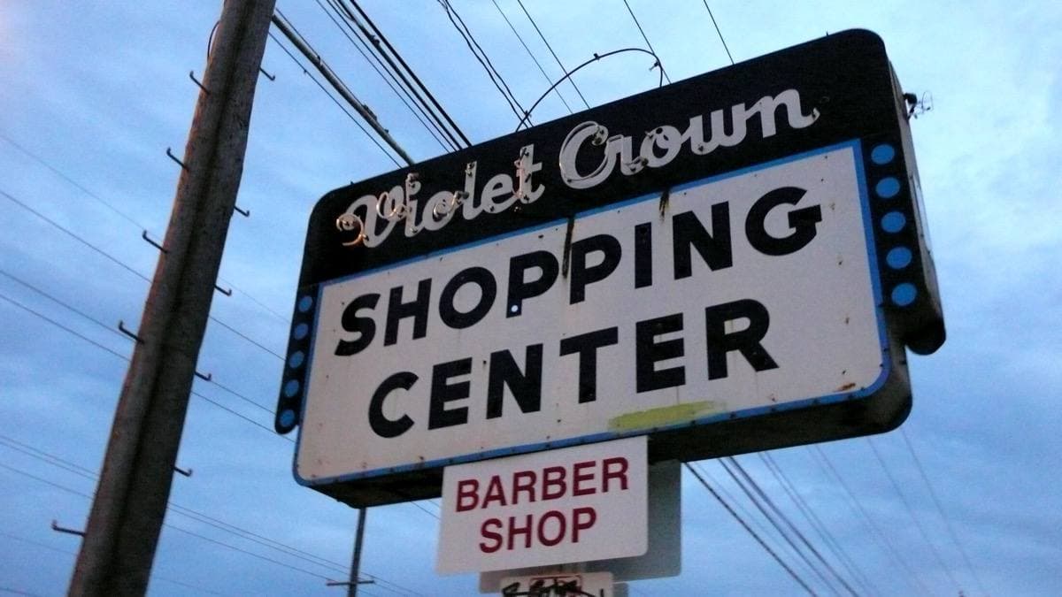 A vintage sign reading Violet Crown Shopping Center, with a smaller barber shop sign below