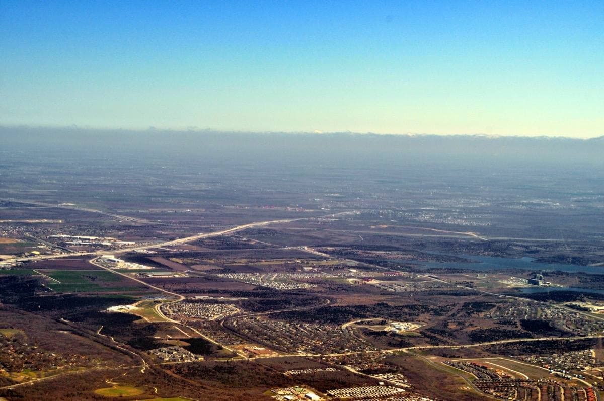Aerial view of flat land east of Austin with a lake towards the horizon