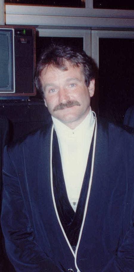 Robin Williams in a dark velvet jacket and white scarf, smiling, 1990