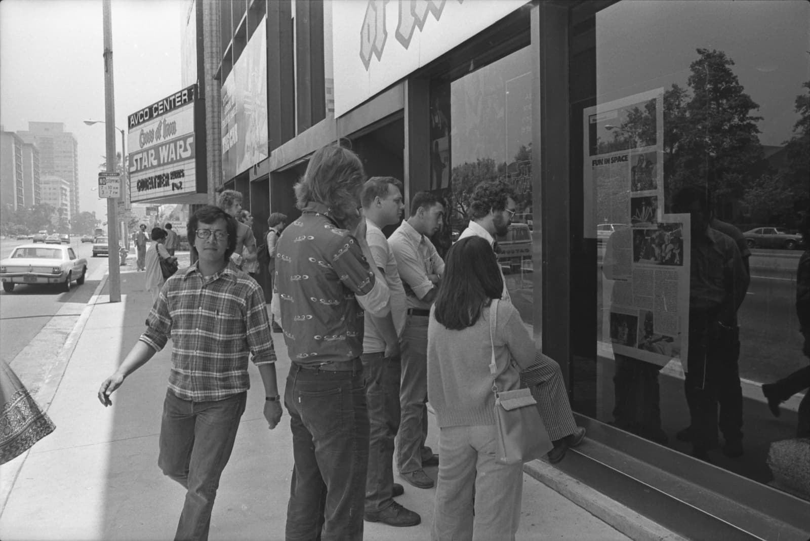 People reading a newspaper article posted outside a cinema