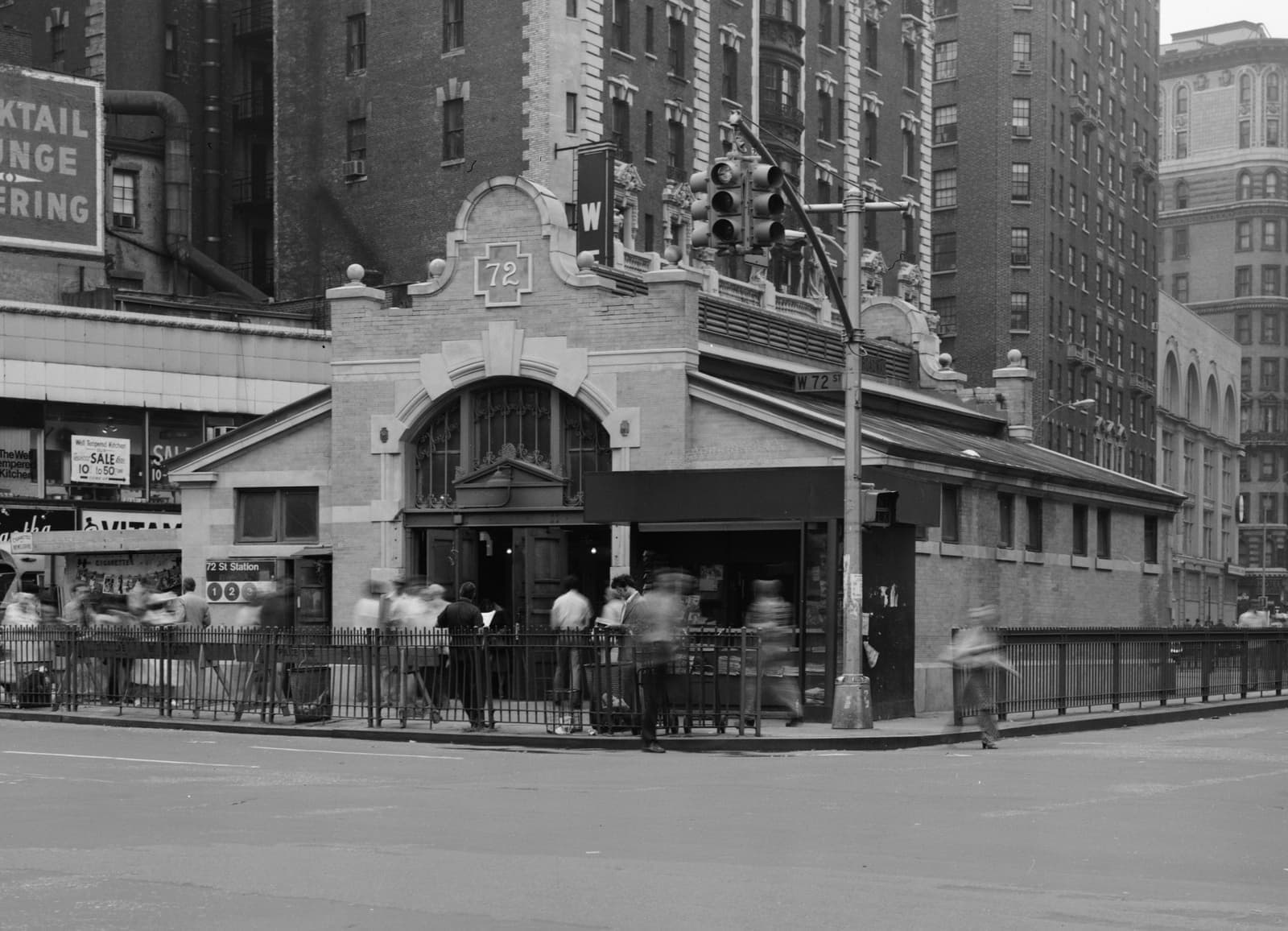 An ornate brick-and-limestone subway entrance pavilion on a traffic island
