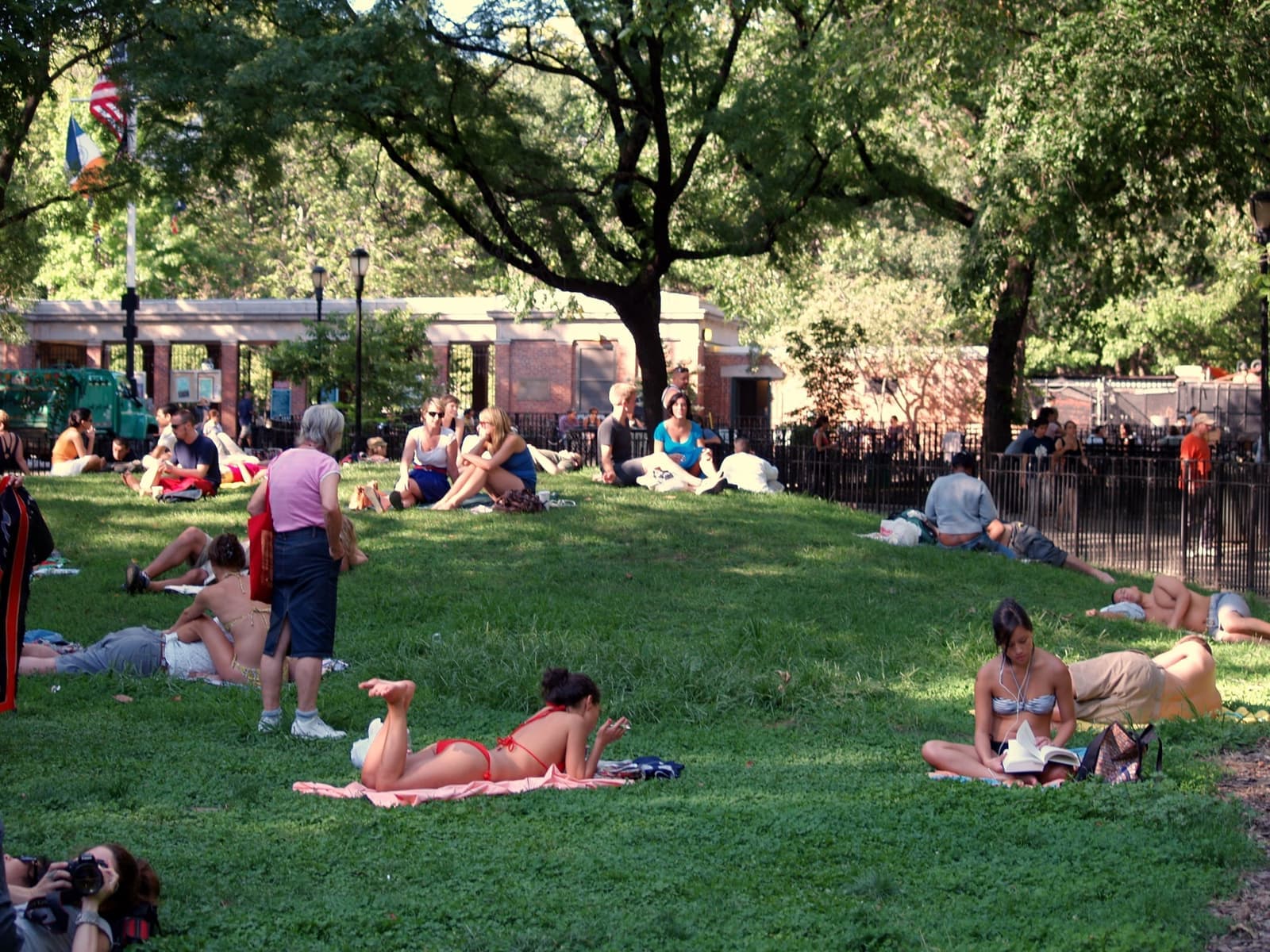 People relaxing on a grassy knoll under big trees