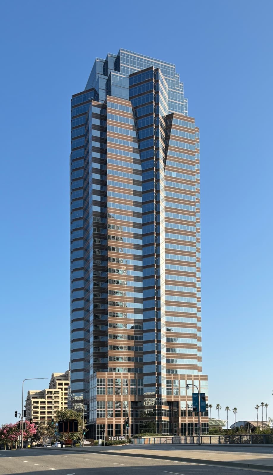 A tall tower of tinted glass and pink granite bands under a clear blue sky
