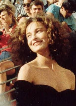 Jennifer Grey with long curly dark hair, smiling, in a black off-the-shoulder dress