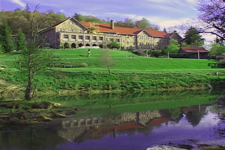 A stone hotel on a green slope reflected in still water at the foot of the lawn