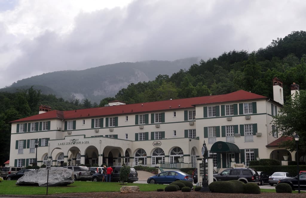 A long cream-coloured inn with a red roof and arched porches below wooded mountains