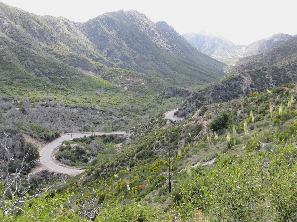 A two-lane mountain road curving through a wide, dry valley