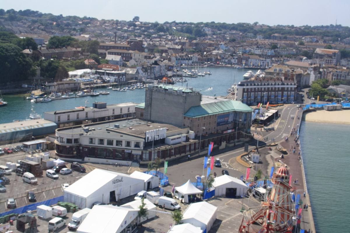 A harbour mouth with a low theatre building on the quay and the town on the hill behind