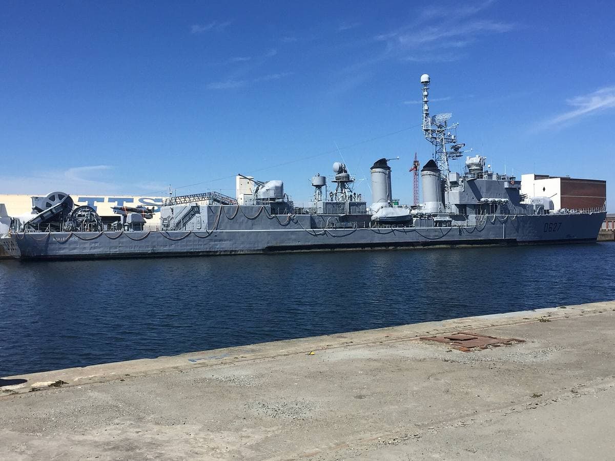 A grey destroyer under tow in a harbour basin