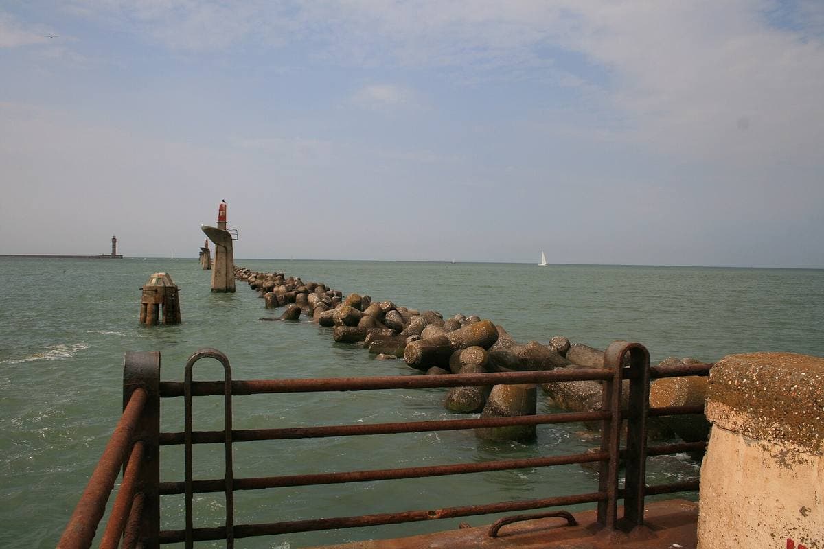 A line of old concrete piles and breakwater blocks running out into green sea from a railing