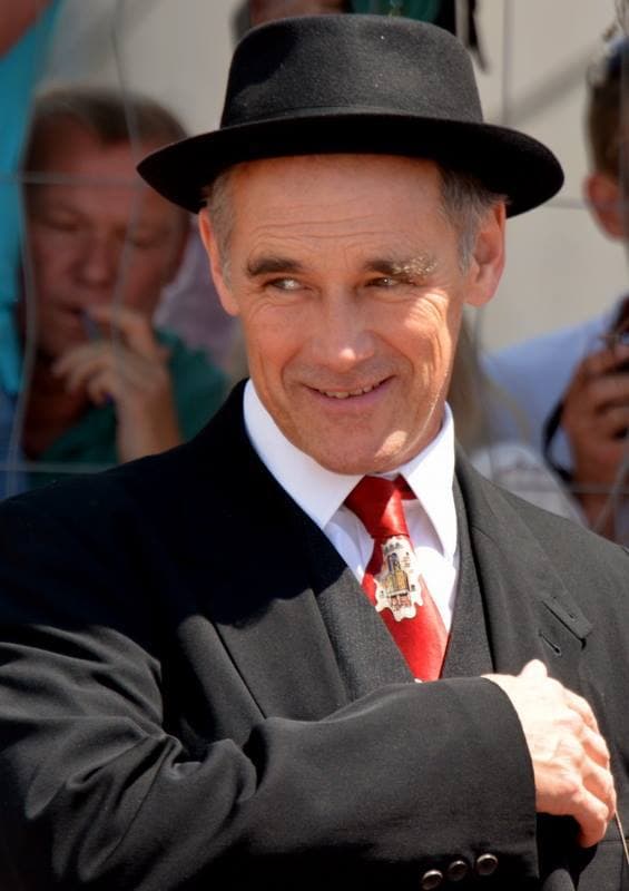 Mark Rylance in a dark hat and jacket, smiling