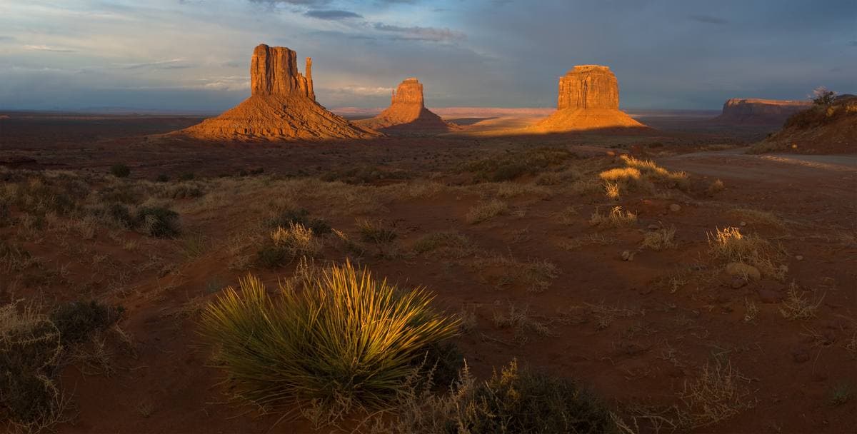 Red buttes lit orange by the setting sun above a dark desert floor