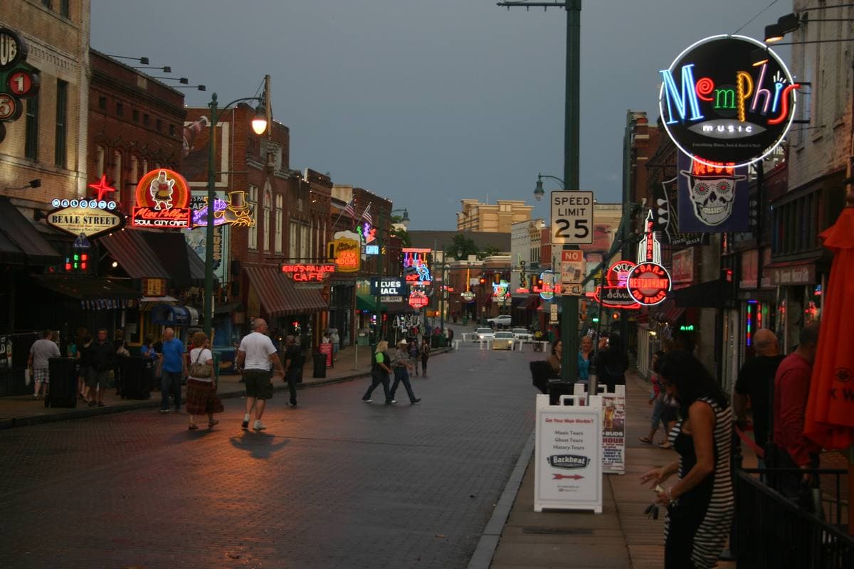 Neon signs and brick club fronts along a pedestrian street at dusk