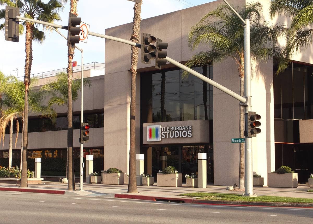 A modern studio office block behind palm trees at a road junction