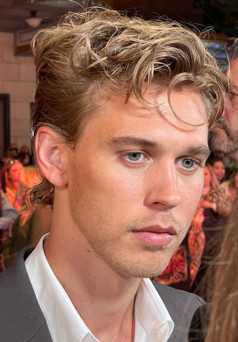 Austin Butler, fair hair falling over his forehead, on a red carpet at night