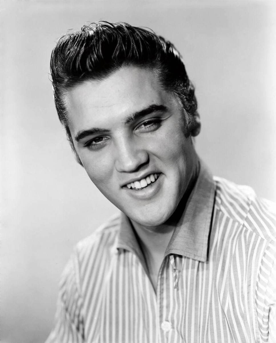 Black-and-white portrait of a smiling young Elvis Presley with swept-back hair
