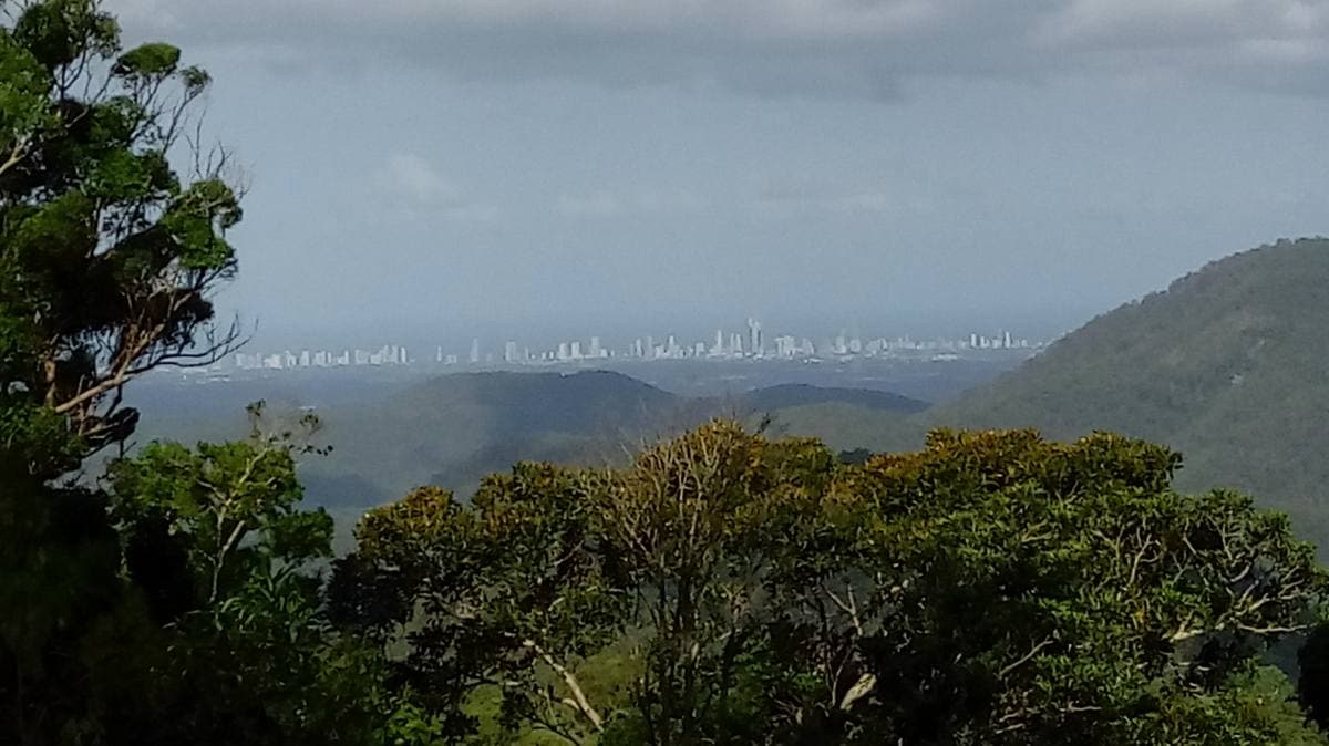 Forested hills falling away towards a distant line of coastal towers