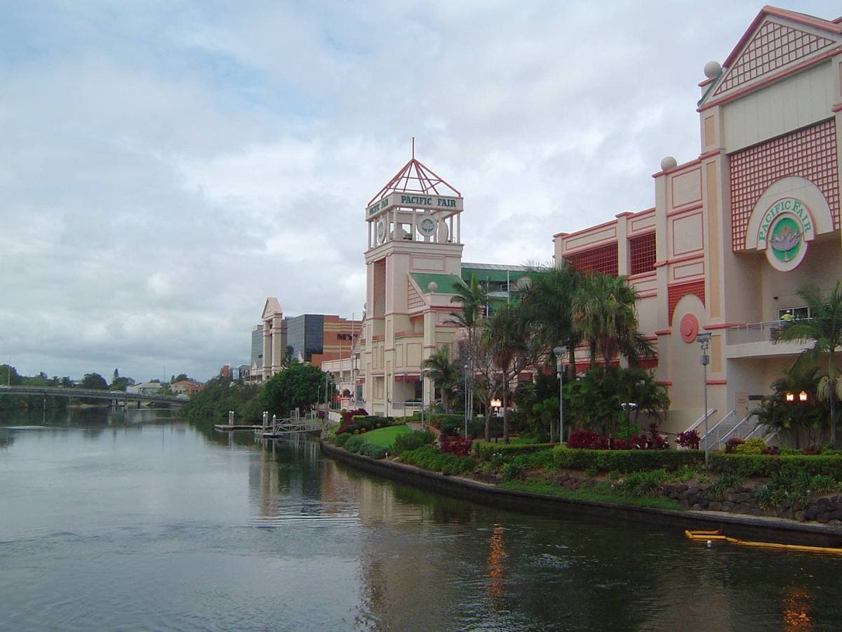 A pastel shopping-centre tower and palm-lined bank reflected in a creek