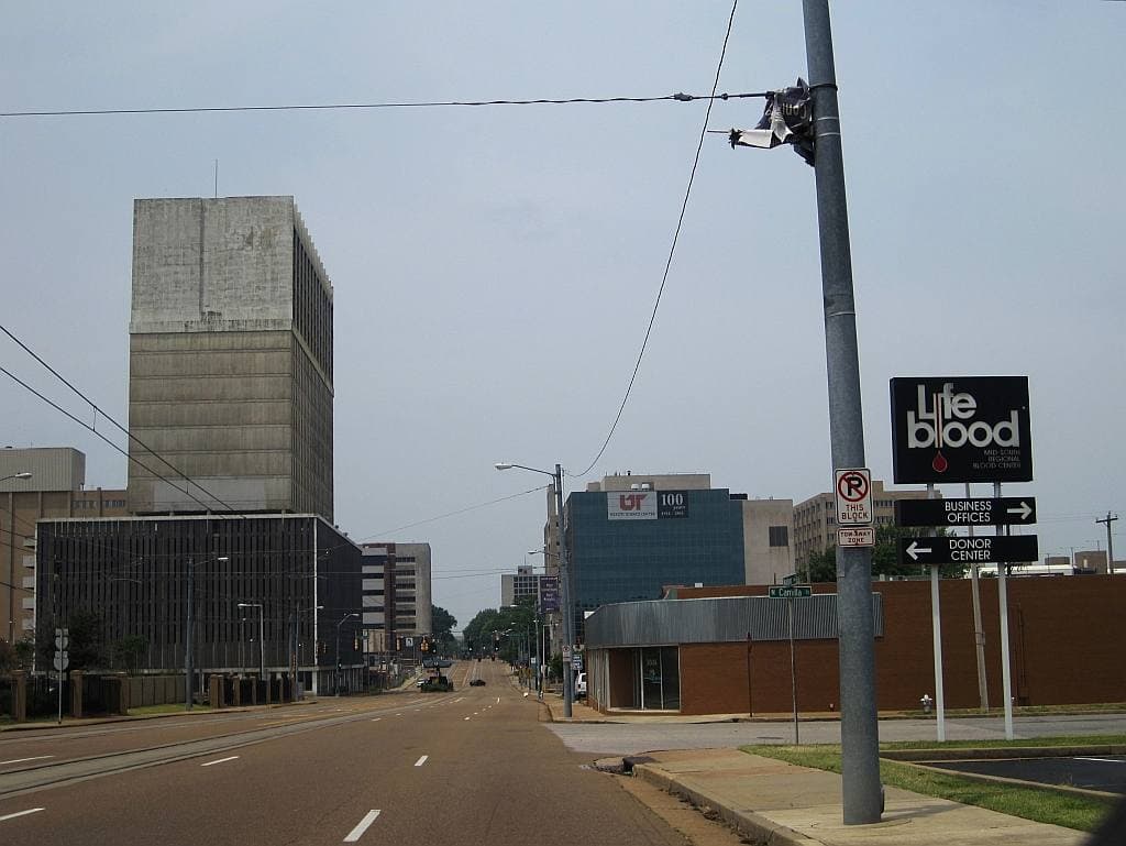 A wide empty avenue with low medical buildings and a concrete tower