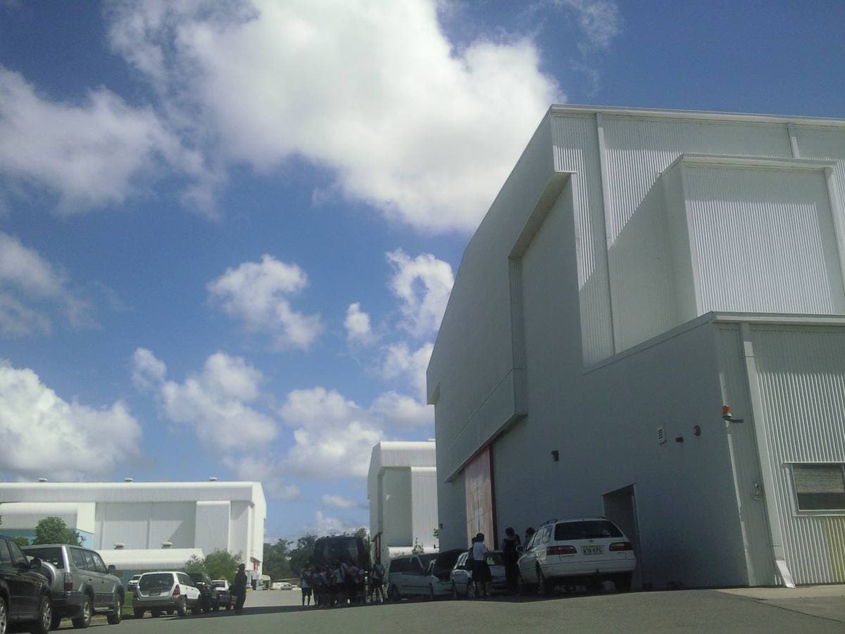 Tall white sound-stage buildings with cars parked along a studio road under a blue sky