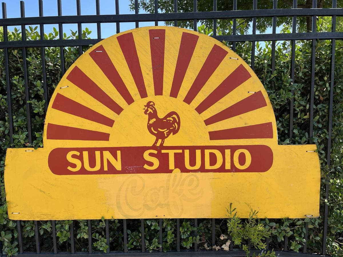 A small brick corner building with a striped awning and a giant guitar sign
