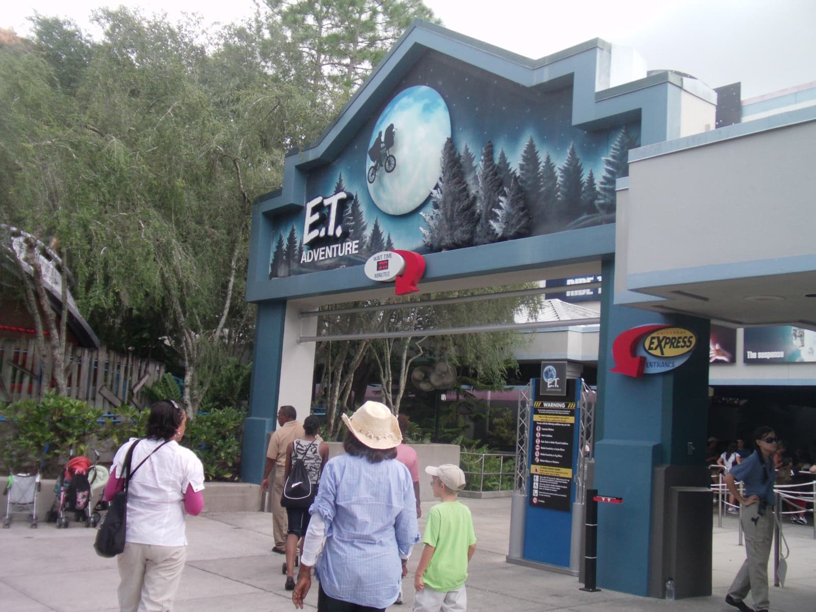 Visitors walking under a blue ride entrance with painted pine trees and a full moon
