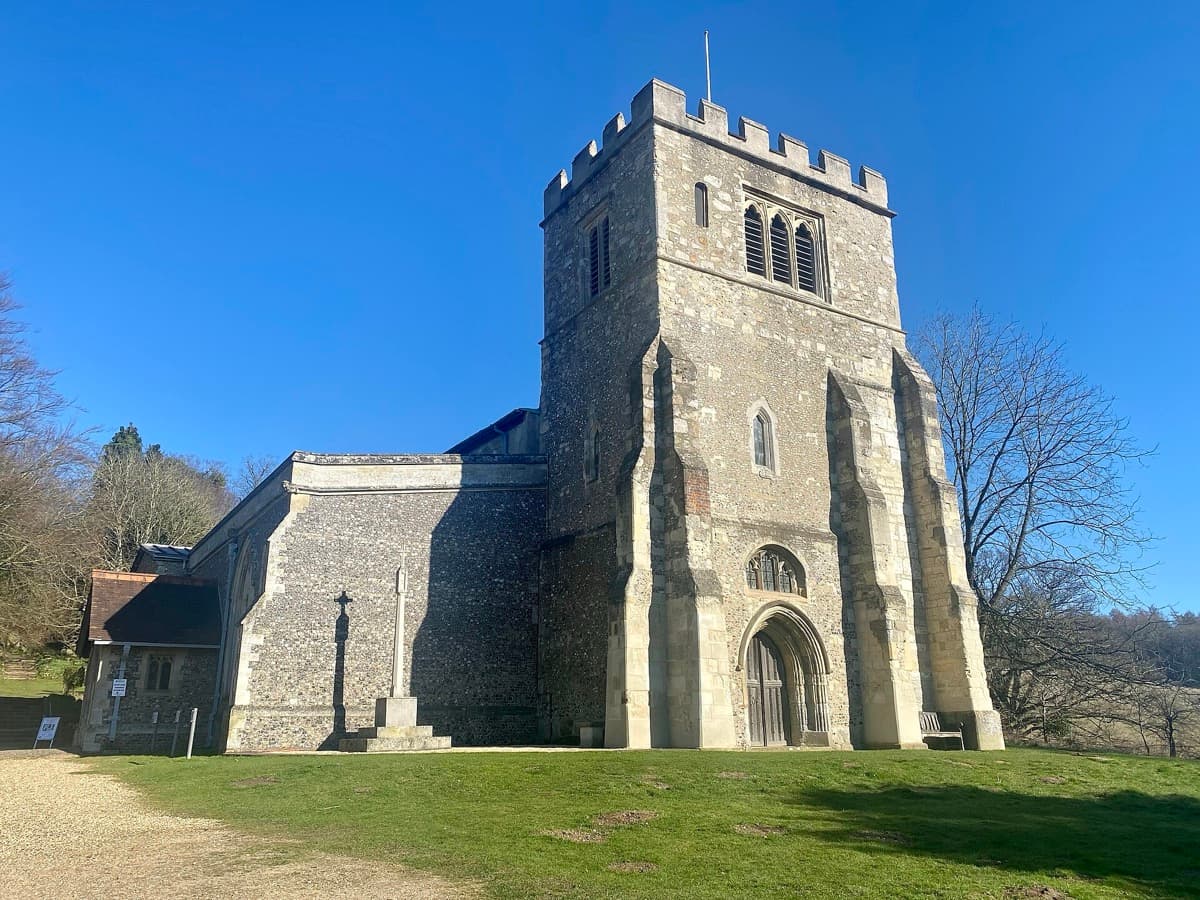 A flint parish church with a square tower seen across its churchyard