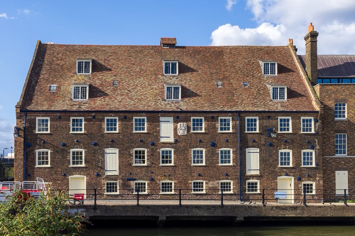 A tall brick tidal mill with a tiled roof beside a river
