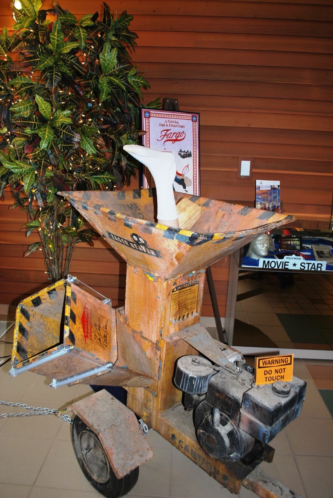 A battered orange woodchipper on a tiled floor, a stuffed sock poking out of its chute