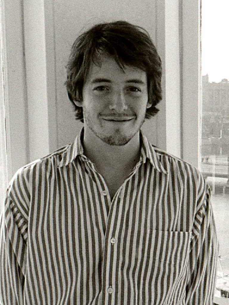 Matthew Broderick at 24, in a striped shirt, smiling slightly beside a window, black and white